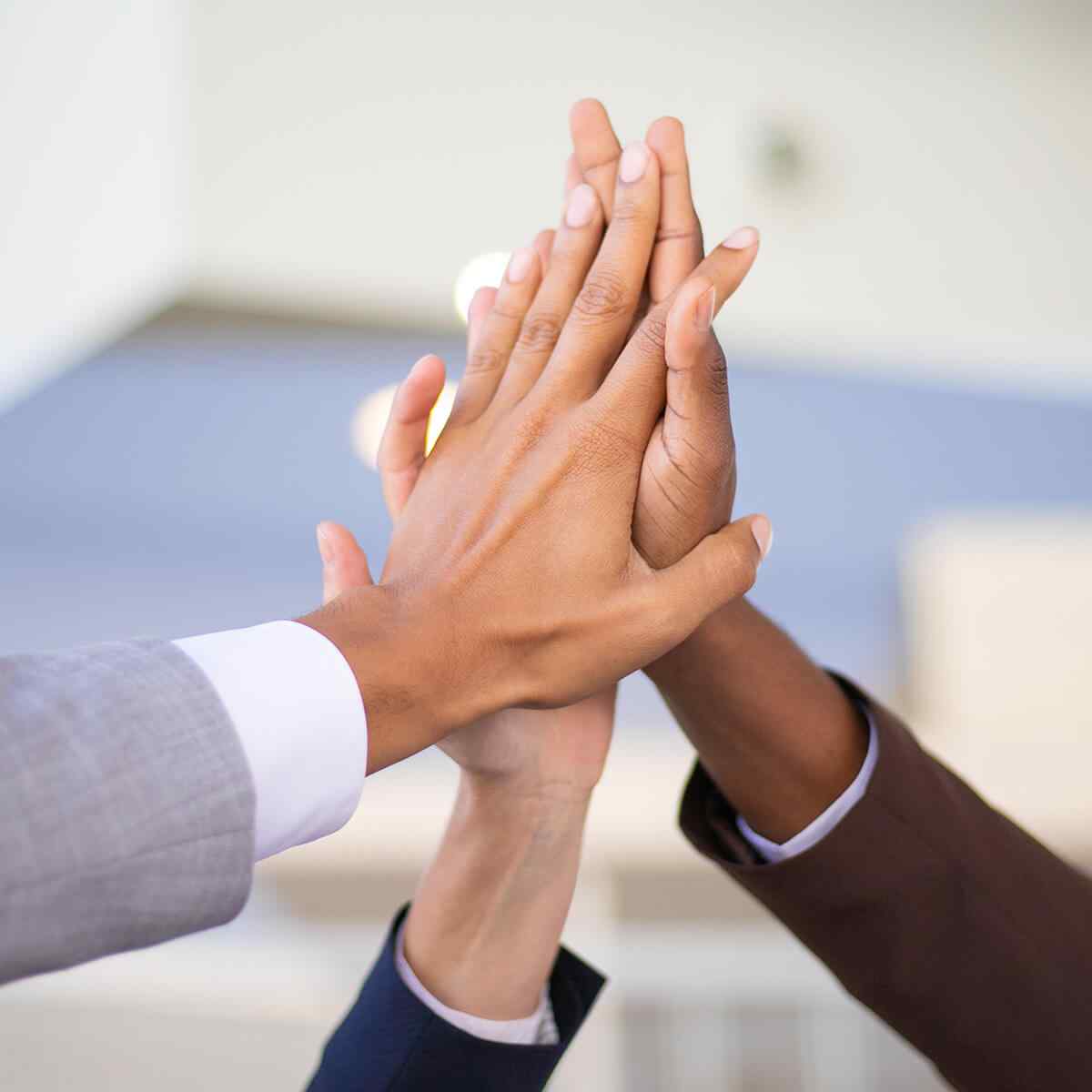 Business colleagues celebrating success and joining hands. Multiethnic group of man and women giving high five to each other. Achievement concept